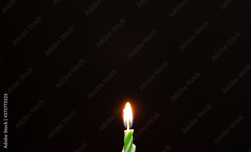 Green birthday candle. Birthday candle on black background. Burning birthday candle on black texture. Green birthday candle. Birthday candle on black background. Burning birthday candle on black texture.