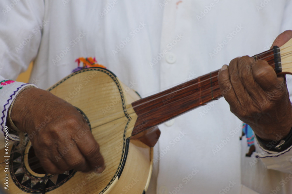 hands of a man playing a wooden guitar with white clothes and Mexican decorations