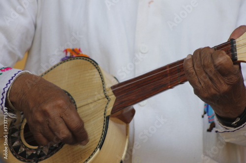 hands of a man playing a wooden guitar with white clothes and Mexican decorations