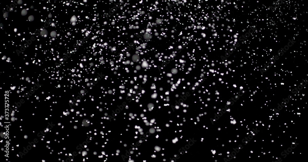 Cloud of white snowflakes floating in the air. The shiny flakes are falling slowly from the sky against an isolated black background