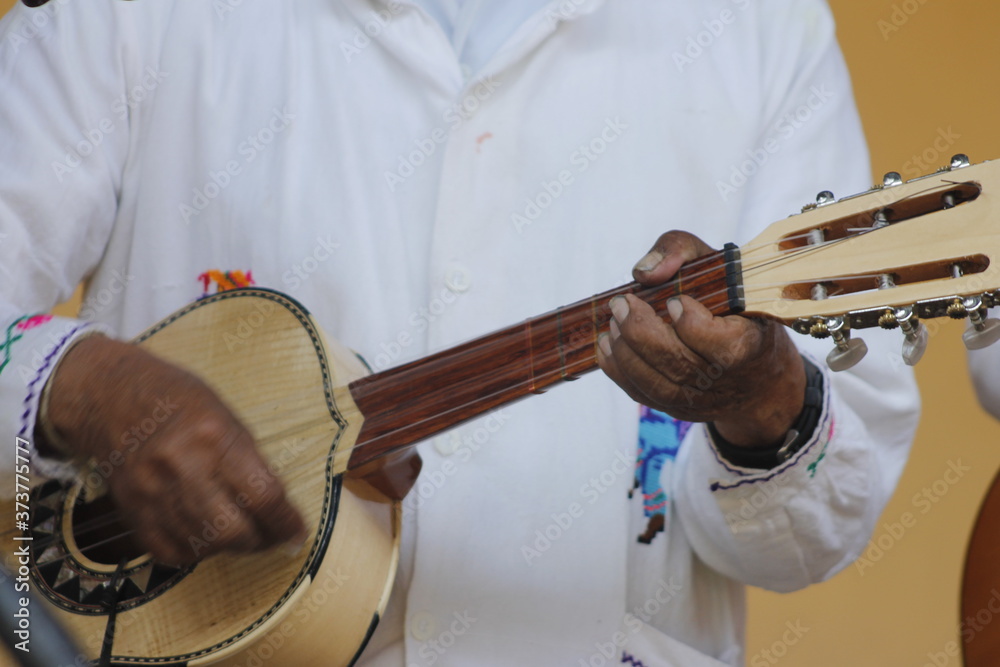 hands of a man playing a wooden guitar with white clothes and Mexican decorations