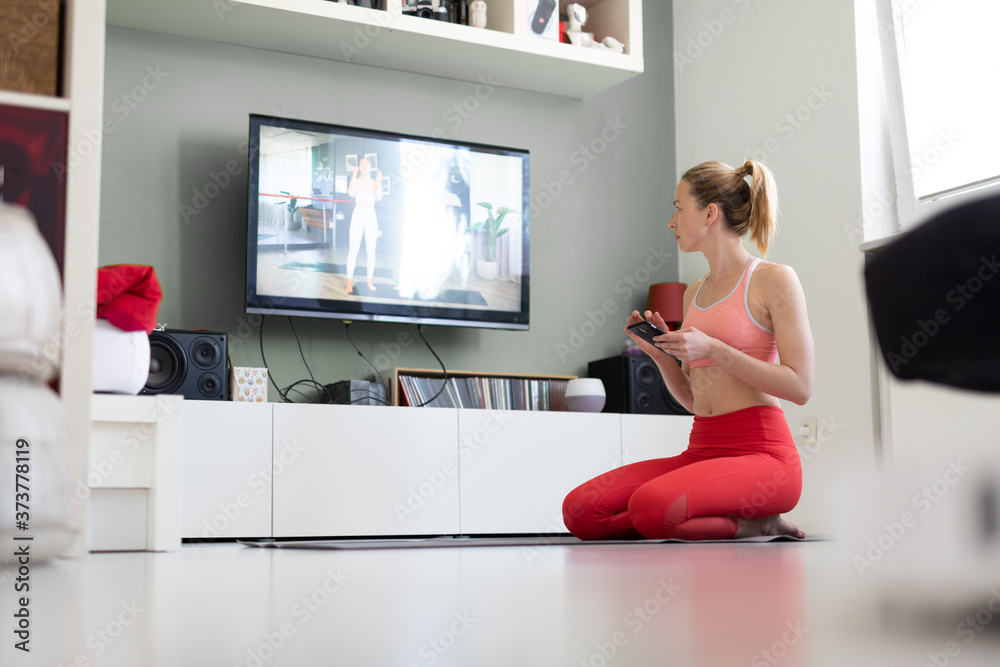 Attractive sporty woman working out at home, doing pilates exercise in front of television in small studio appartment. Social distancing. Stay healthy and stay at home during corona virus pandemic. Attractive sporty woman working out at home, doing pilates exercise in front of television in small studio appartment. Social distancing. Stay healthy and stay at home during corona virus pandemic.