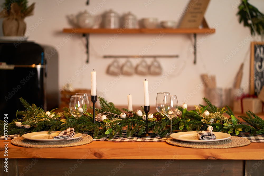 The festive Christmas table is decorated with branches of a Christmas tree, candles and garlands. Cozy home Christmas atmosphere.