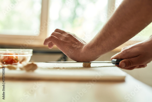 Close up of hands of man, chef cook cutting garlic on the chopping board while preparing a meal in the kitchen