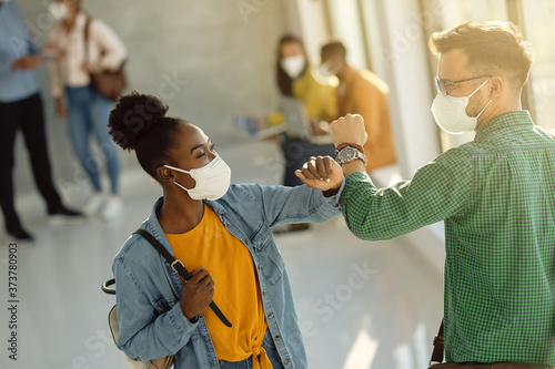 Happy university students greeting with elbow while wearing protective face masks. photo