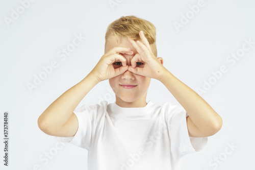 A portrait of a schoolboy who put his hands to his eyes - shows binoculars. Isolated background.