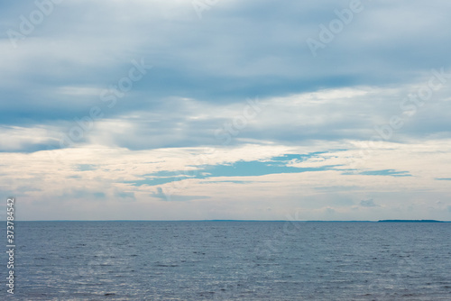 Deep cold blue water of Ladoga lake with sun light reflections under blue cloudy sky