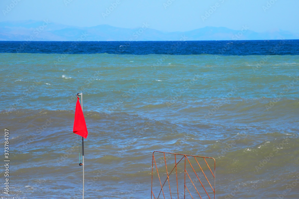 The beach is closed Storm at sea. Red flag prohibiting swimming on the beach.