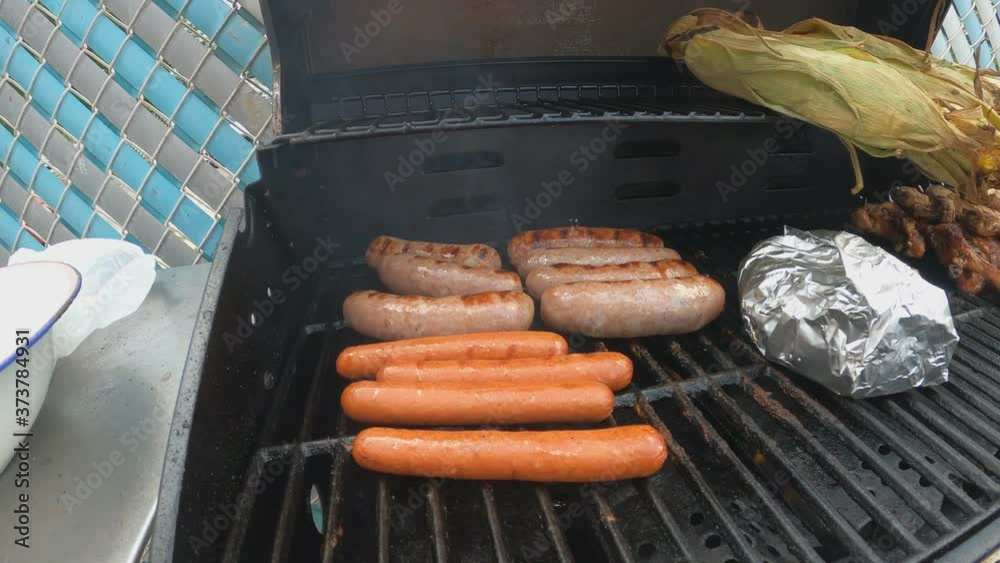 Hand hold shot of hot dogs and bratwurst sausage being barbecued