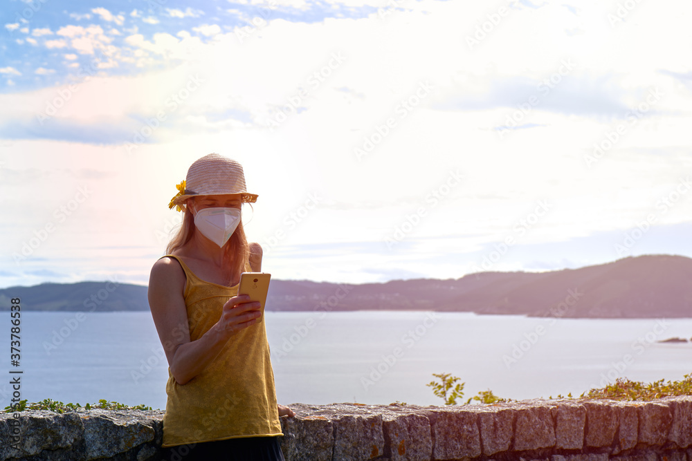 Young woman with a protective mask using a smartphone on vacation in a lookout point. The new concept of normality.