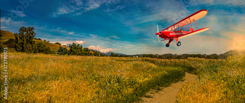 Vintage bi-plane flying over golden harvest fields at dawn landscape.