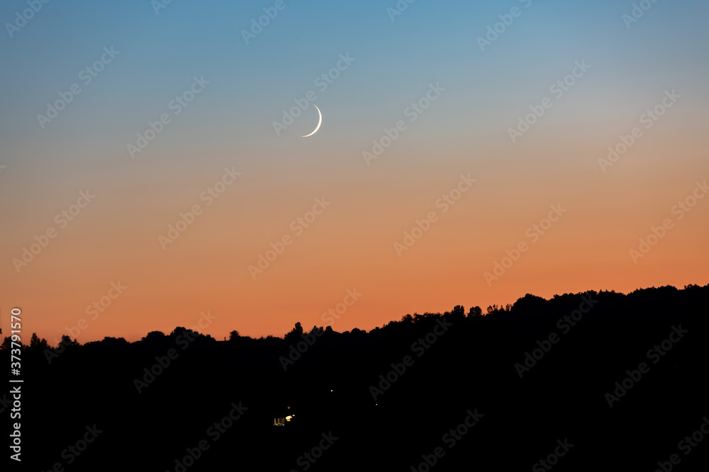 A young moon on an orange-blue sunset sky over a dark forest. Horizontal orientation. High quality photo A young moon on an orange-blue sunset sky over a dark forest. Horizontal orientation. High quality photo