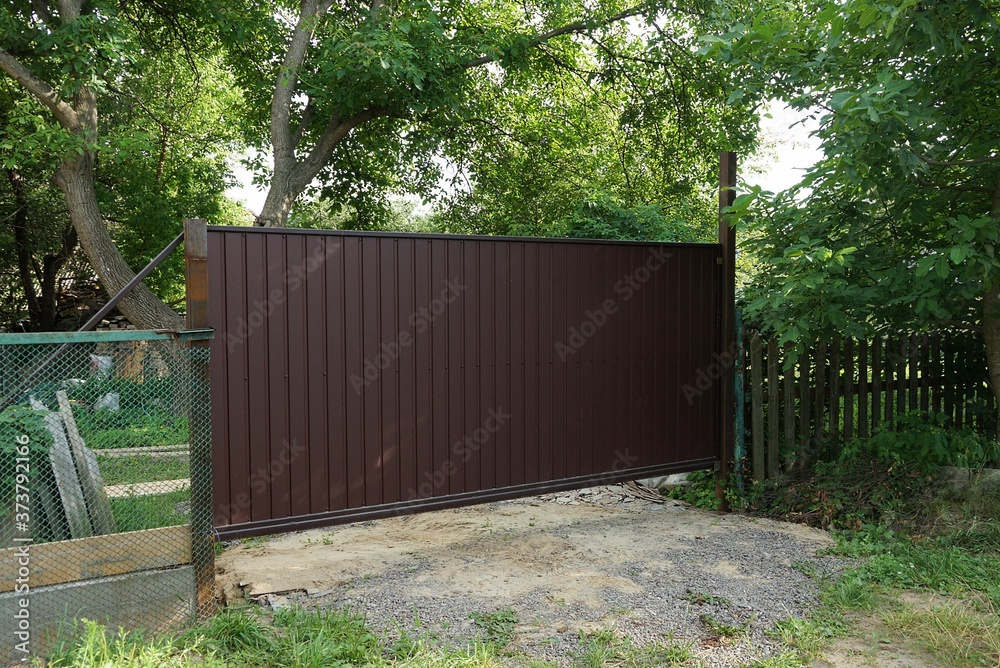 one big closed brown metal gate and part of the fence on the street in green grass