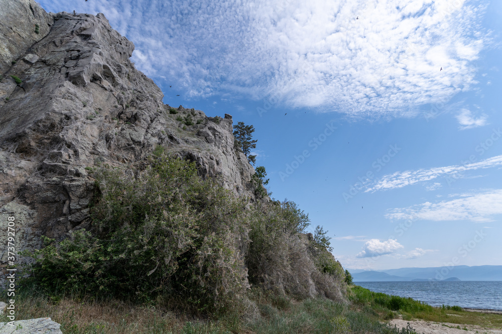 Russia, Irkutsk region, Olkhon, July 2020: cliff cave near baikal lake, low angle view, stunning blue cloudy sky