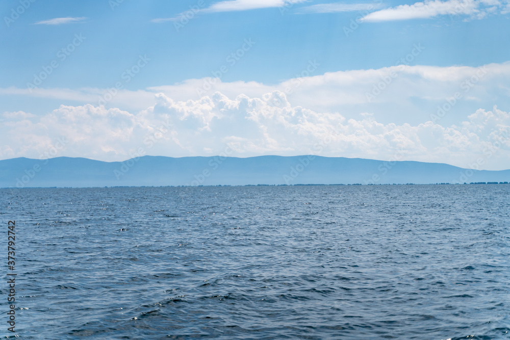 Russia, Irkutsk region, Baikal lake, July 2020: scenic landscape of smooth lake water with wooly cloudy above Russia, Irkutsk region, Baikal lake, July 2020: scenic landscape of smooth lake water with wooly cloudy above