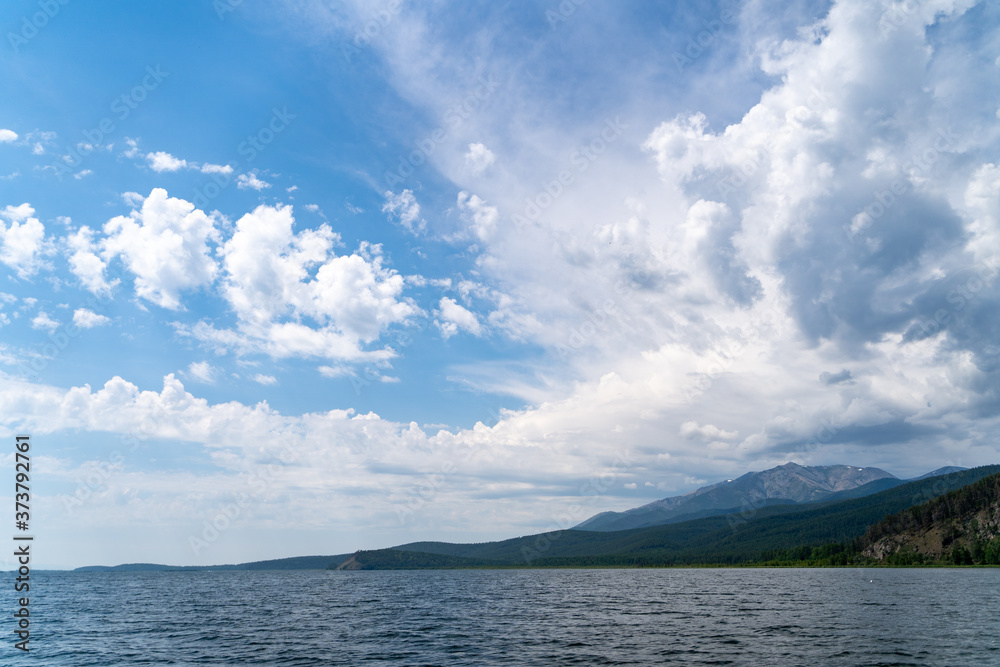 Russia, Irkutsk region, Baikal lake, July 2020: scenic landscape of smooth lake water with wooly cloudy above