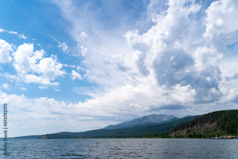 Russia, Irkutsk region, Baikal lake, July 2020: scenic landscape of smooth lake water with wooly cloudy above