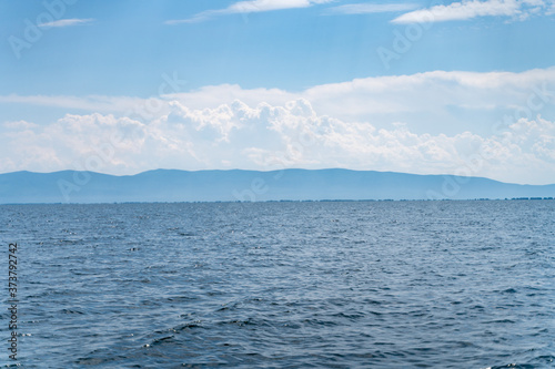 Russia, Irkutsk region, Baikal lake, July 2020: scenic landscape of smooth lake water with wooly cloudy above photo