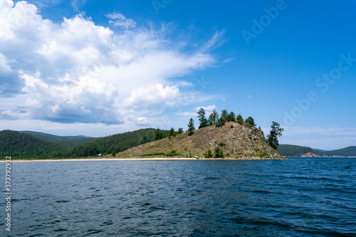 Russia, Irkutsk region, Baikal lake, July 2020: yellow sand cliff with rare trees in the lake