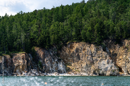Russia, Irkutsk region, Baikal lake, July 2020: stone mountains with evergreen forest on them, from water view