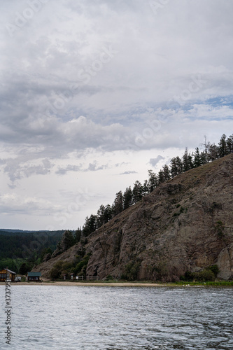 Irkutsk region, Olkhon, Baikal lake, July 2020: summer on russian north, cloudy sky and ricky cliff with forest on it photo