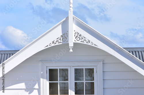 Roof top of classic white wooden villa with multi pane window and carved finial.