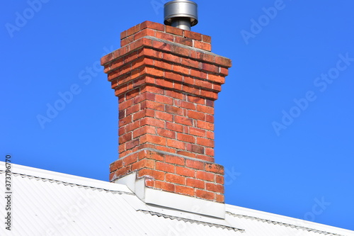 Fotografia Vintage red brick chimney with modern metal lining on top of white corrugated sheet metal roof