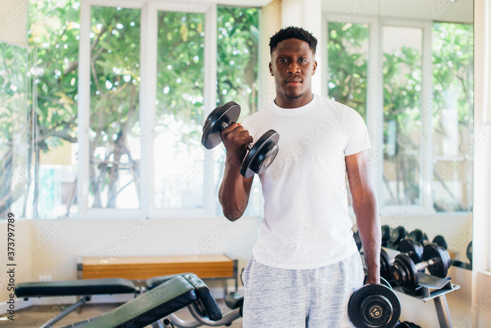 Young African American man standing and lifting a dumbbell with the rack at gym. Male weight training person doing a biceps curl in fitness center Young African American man standing and lifting a dumbbell with the rack at gym. Male weight training person doing a biceps curl in fitness center