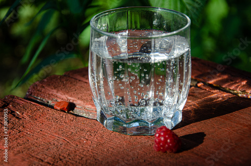 A glass with mineral, carbonated water raspberry berry, on a wooden board in the garden.