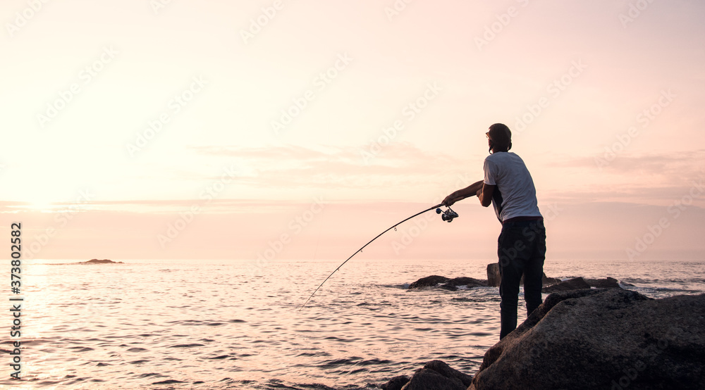 Young professional fisherman casts his rod (spin technique), trying to fish while the sun goes down in a good fishing point of northwest of Spain, next to Portuguese border.