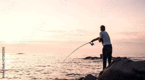 Young professional fisherman casts his rod (spin technique), trying to fish while the sun goes down in a good fishing point of northwest of Spain, next to Portuguese border.