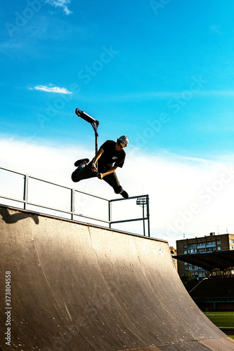 The teenager on the scooter in a jump against the background of the sky. Backlight.