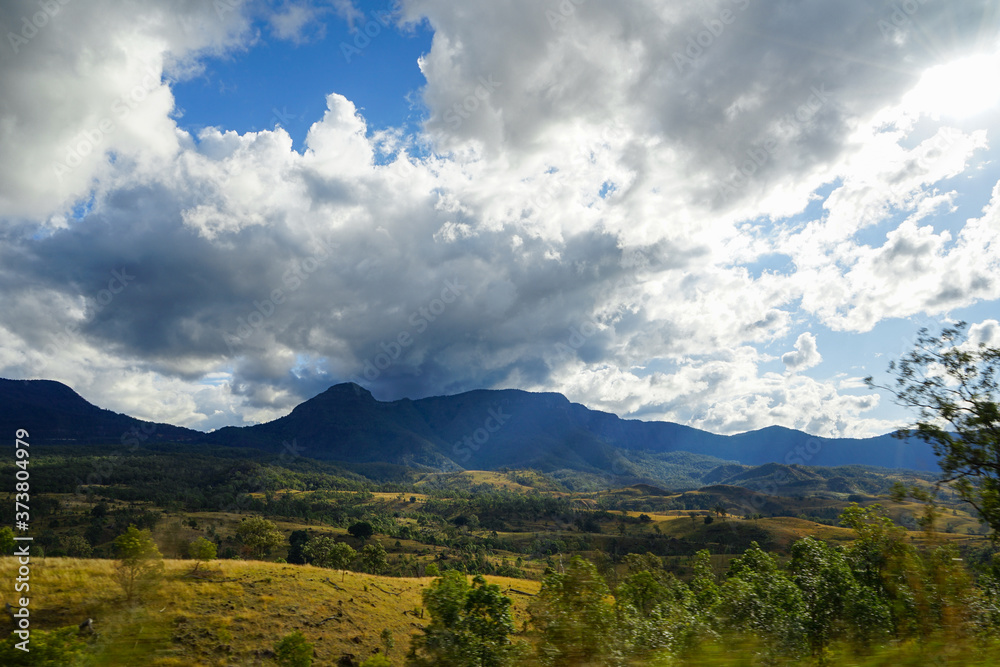 Dramatic dark clouds over distant blue mountain; Motion blur in the foreground; Golden hills illuminated by afternoon sun.