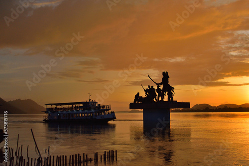 Silhouette of Lachit Borphukan statue during sunset with a ship passing in background in river brahmaputra.	 photo