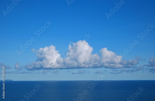 View of a calm blue sea with white fluffy clouds and clear blue sky on a sunny day in early morning .