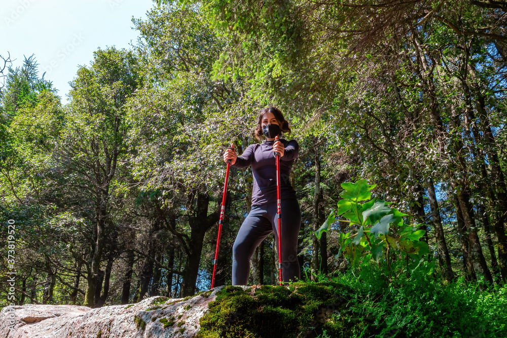 woman walking through a natural environment with the walking stick and her mask