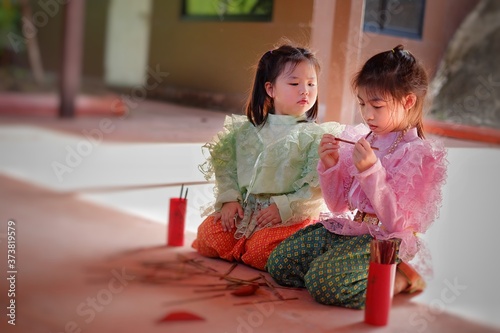 Cute young Asian girls in traditional Thai costumes are shaking chi-chi sticks, also known as Kau chim . or Kau cim sticks during a festive Thai new year festival called Songkran.