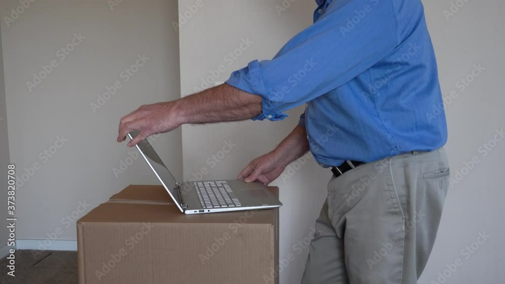Close up of senior man dressed for work typing on laptop set stack of boxes in empty apartment. Finishes typing, closes computer and leaves room.