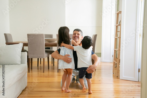 Laughing father hugging adorable little kids at home. Happy attractive Caucasian dad embracing lovely children, smiling and playing with them. Fatherhood, leisure and parenthood concept