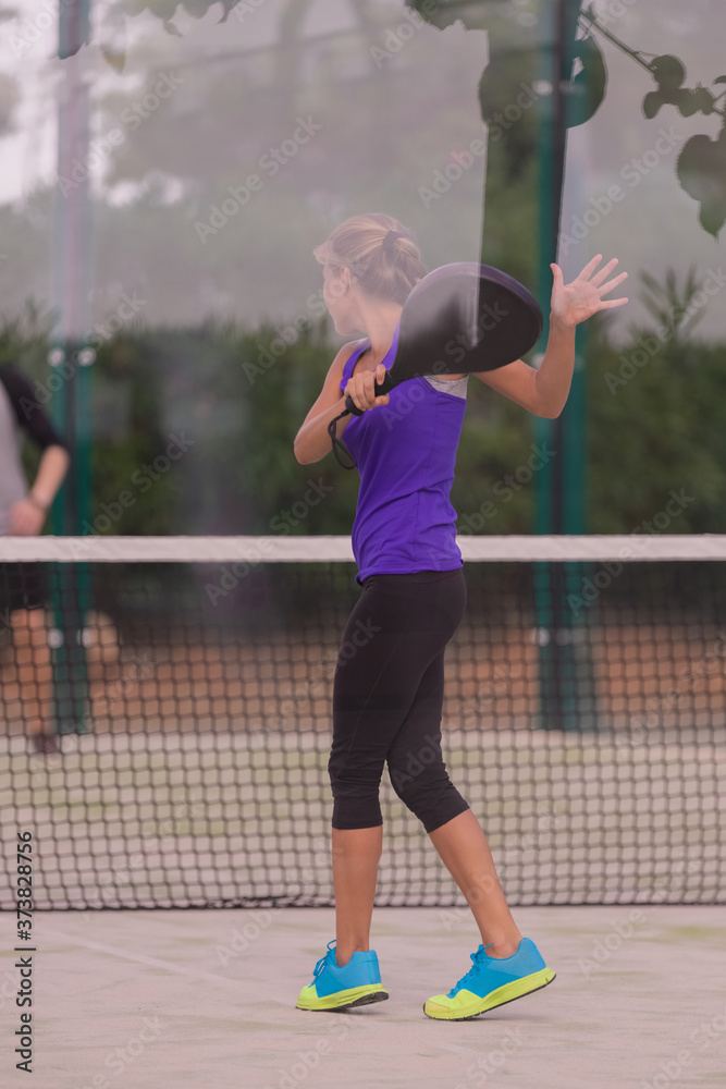 Woman holding a paddle racquet after returning a shot at a paddle court on an out of focus background. Paddle and lifestyle concept.