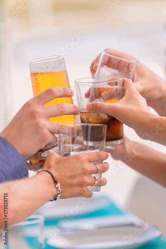 Close up of an assortment of hands doing a toast with different drinks on an out of focus background. Friendship and lifestyle concept.