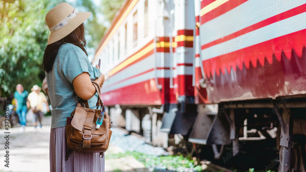 Obraz premium Mini portable alcohol gel bottle to kill Corona Virus(Covid-19) hang on leather shoulder bag of woman at railway staion. New normal lifestyle. Health care concept. Selective focus on alcohol gel