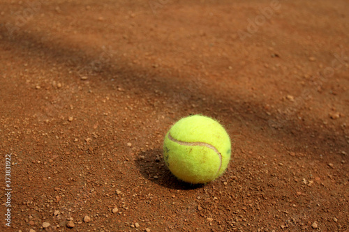 Close up of tennis ball on clay court. Tennis ball on a tennis clay court. Red clay tennis court. Sand on a court.