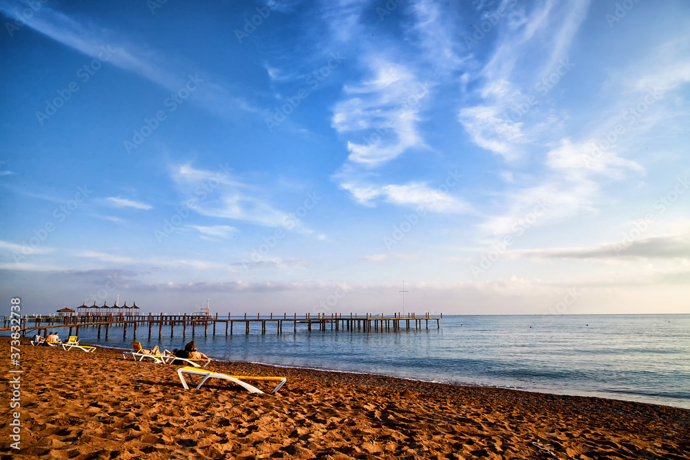 Obraz premium View from sand beach to water of sea, pier and silhouette of people or tourists in a nice day or evening with blues sky and white clouds.