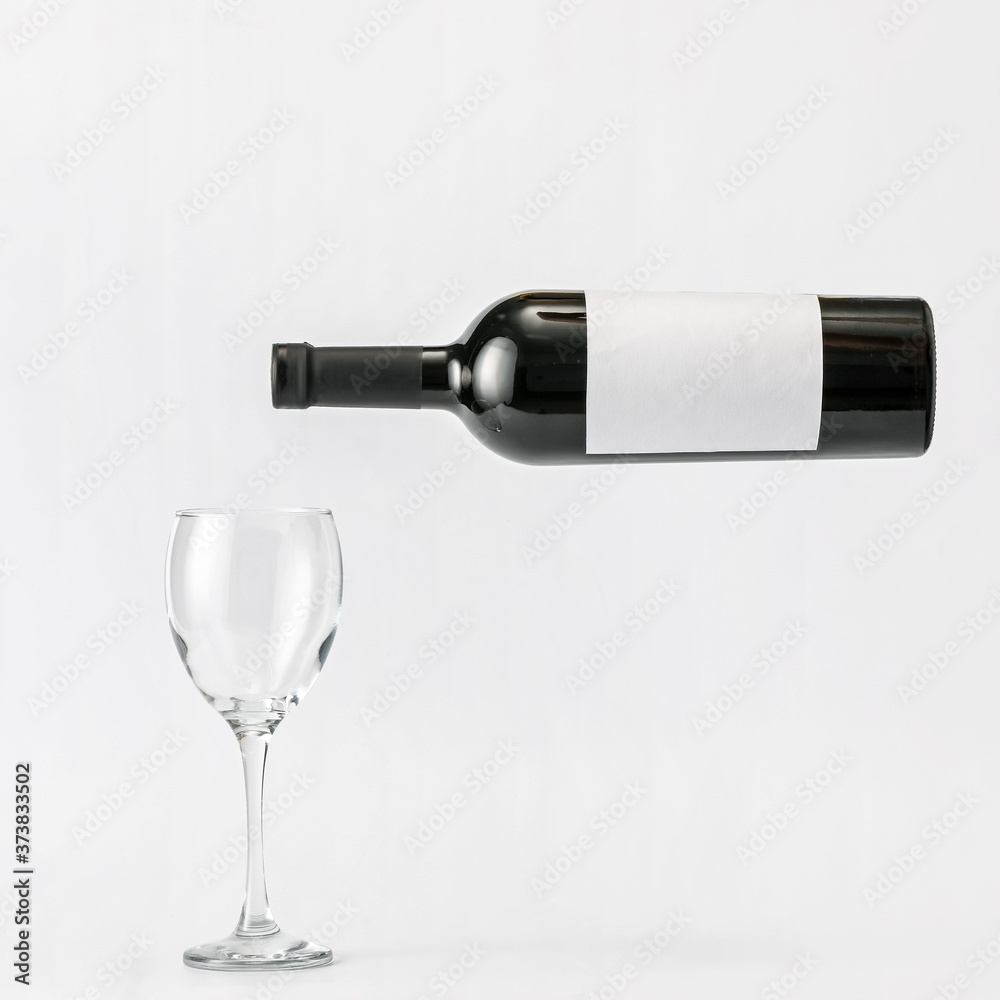 Fototapeta premium Bottle of wine with blank label and glass on light background