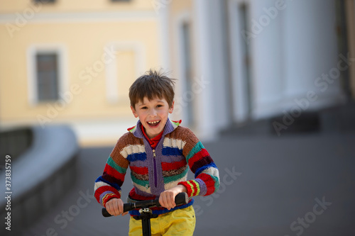 The child is holding the wheel of the scooter. Cheerful boy on a walk in the street.