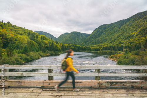 Hiker woman with backpack walking on bridge crossing river. Motion blur of tourist hiking in outdoor nature fall. Autumn traveling hike in Quebec, Canada.