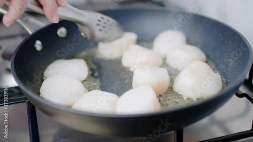 Close-up of frying lots, multiple scallops in oil in a pan on a gas stove in 4K. Concept of cooking fried scallops in slow-motion.