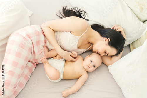 Happy young mother and cute baby in bed. Light background.