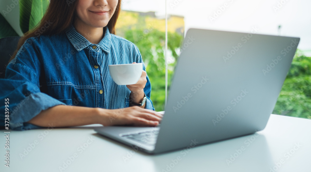 Closeup image of a woman working and typing on laptop computer while drinking coffee in office Closeup image of a woman working and typing on laptop computer while drinking coffee in office